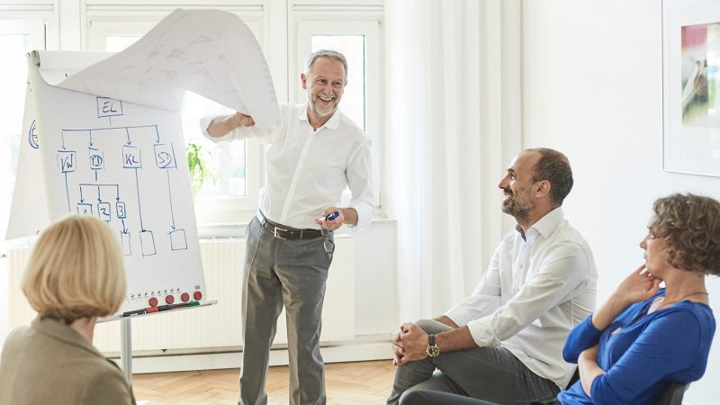 Organisationsberatung nach den Qualitätskriterien der DGSv. Berater vor Flipchart vor einer diversen Gruppe auf Stühlen